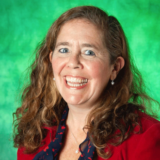 Heidi is facing foward and smiling. She has long wavy brown hair and wears a maroon top.