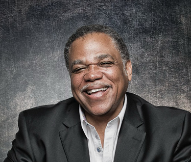 Terence is facing forward and smiling. He wears a white shirt and dark jacket.