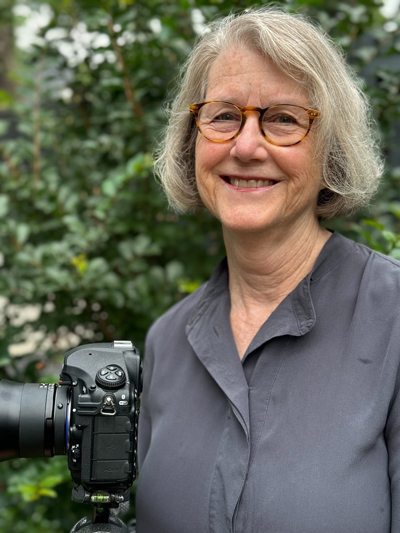 Dornith faces forward and smiles. She wears a gray shirt and glasses.