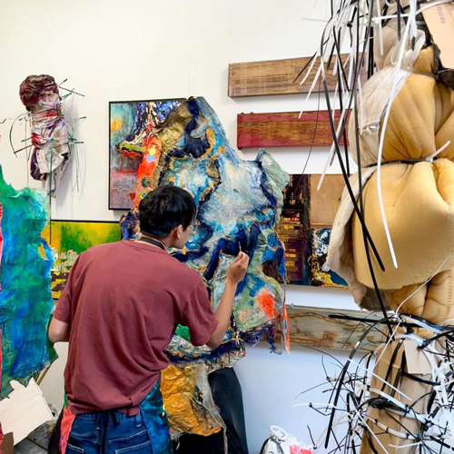 Student in a maroon shirt painting on a canvas.