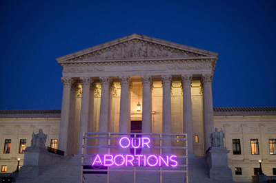 Supreme Court Bldg with "our abortions" in pink neon light