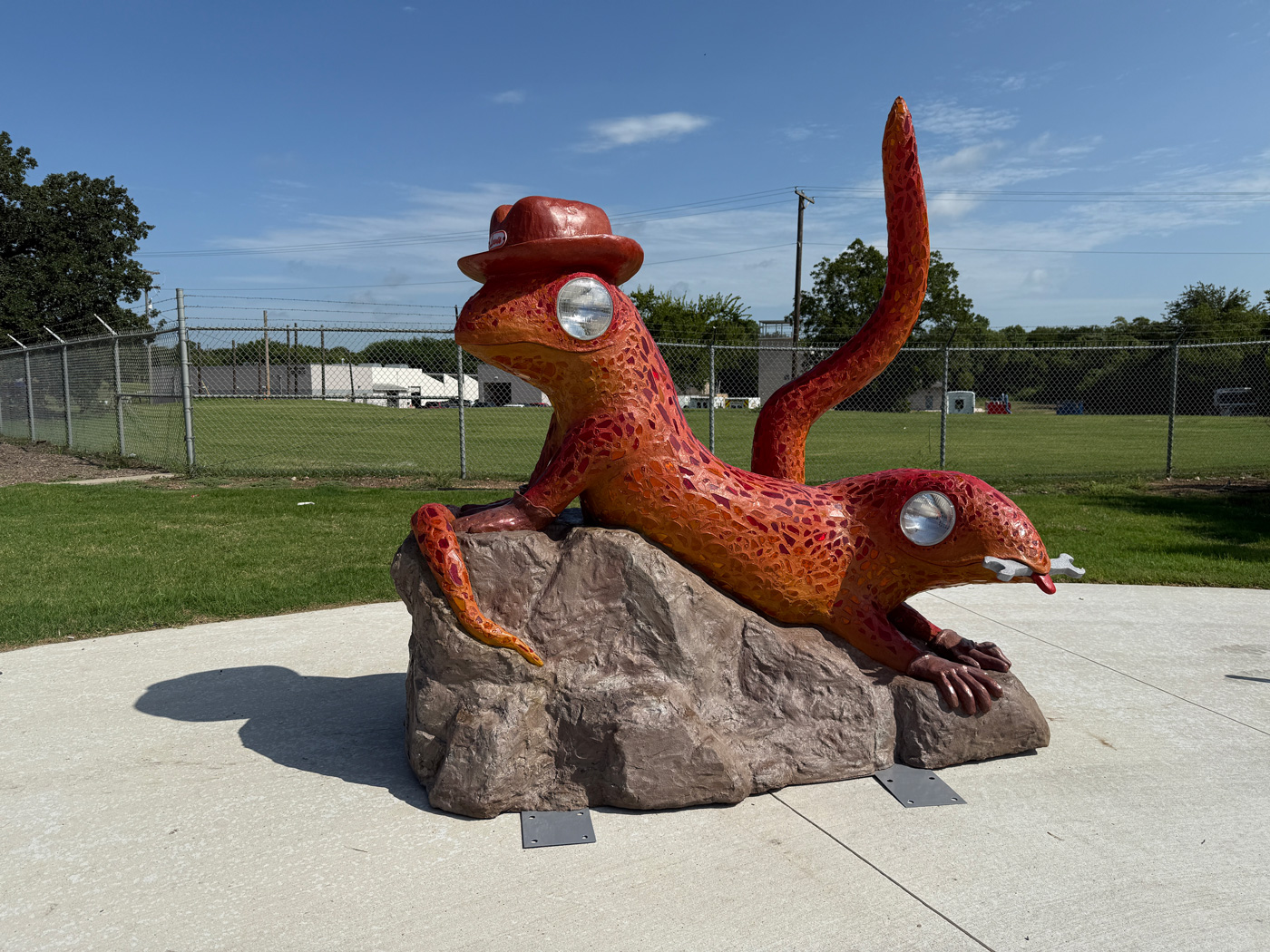 Rust-colored mosaic sculpture of a lizard wearing a hat that says "Lewis"
