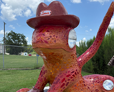 Rust-colored mosaic sculpture of a lizard wearing a hat that says "Lewis"