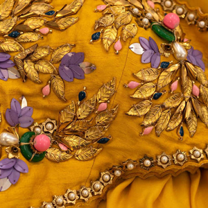 Detail of intricate embroidery and beading on yellow chiffon fabric.