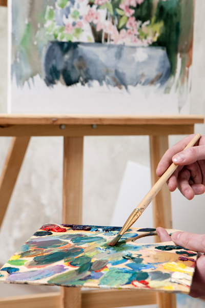 An unfinished painting on an easel, paints and a brush