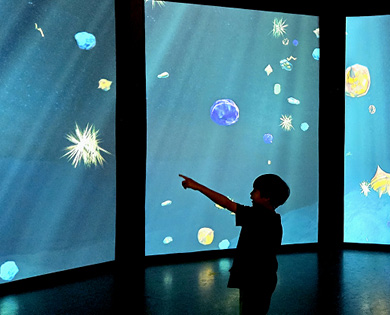 Child pointing at a large screen that displays bodies from outer space.