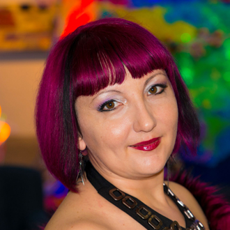 Adela facing forward, smiling, short purple hair, colorful background.