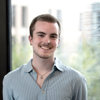 Blake Butterfield headshot in a blue vertically striped button up shirt smiling.