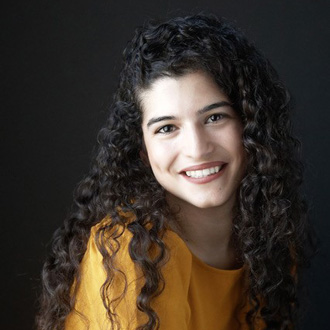 Beatriz facing forward, smiling, long curly hair, yellow top