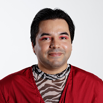 Gomez looking forward, smiling, short dark hair, orange jacket, zebra-patterned shirt