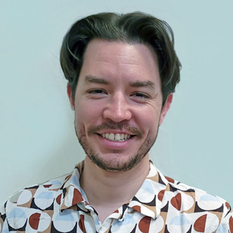 Chris Gonzales facing forward, smiling, short brown hair, brown & white print shirt