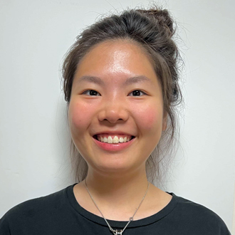 Jingfie facing forward smiling with her dark hair up and wearing a black T-shirt.