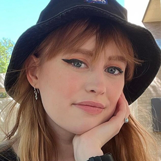 Caitlin resting her chin on her left hand smiling, auburn hair, brown hat.