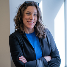 Karen Hutzel facing forward and smiling. She has long wavy brown hair and wears a blue shirt.