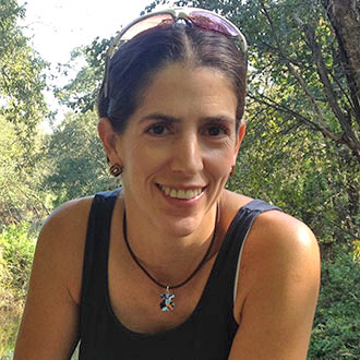 Veronica smiling, hair pulled back, sunglasses atop her head, wearing a sleeveless top, trees in background.