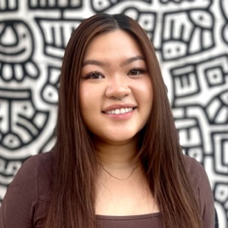 Headshot of An smiling in brown shirt in front of patterned wall