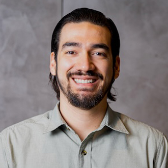 Headshot of An smiling in brown shirt in front of patterned wall