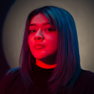 Three-quarter view of Diana looking at the camera with dark red light on her face, dark hair.