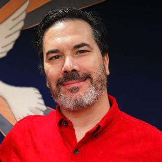 Chris smiling, short black hair with mustache and beard, red shirt