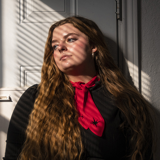 A color head and shoulders portrait of Anna. She wears black with a red scarf around her neck and looks away from the camera to the left.