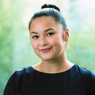 Beatriz Garza headshot. She is wearigna dress, sitting under a tree and smiling. The background is outdoors with a tree trunk visible.