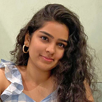 Mnikya with her head tilted facing forward, long curly brown hair, blue and white top