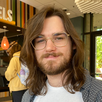 Headshot of An smiling in brown shirt in front of patterned wall