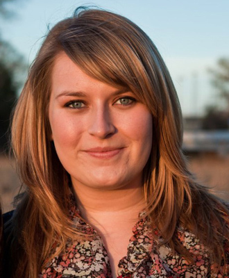 Jaclyn smiling at the camera, long brown hair, flowered print shirt, head and shoulders portrait