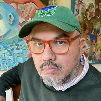 Jorge Lucero facing forward, glasses, wearing a green cap, white shirt under a green sweater