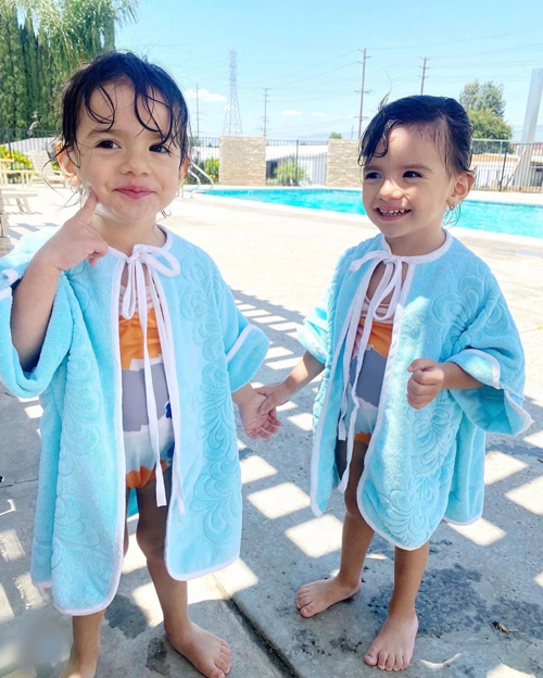 Twin toddlers are standing by a pool, wearing bathing suits and cover-ups that are made from pale aqua vintage towels