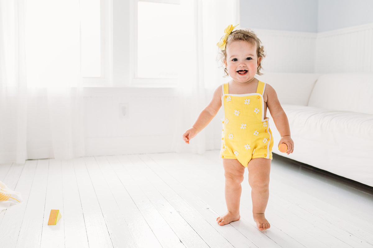 Smiling toddler holds a wooden block wearing a yellow romper