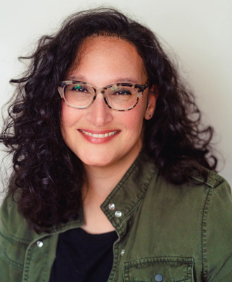 Michele smiling at the camera, long dark curly hair, glasses