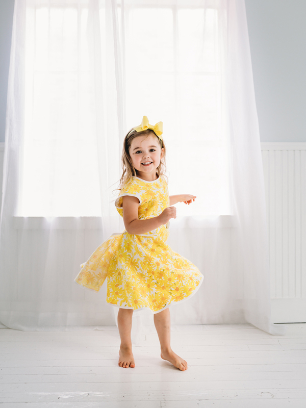 Little girl twirling in a yellow daisy dress