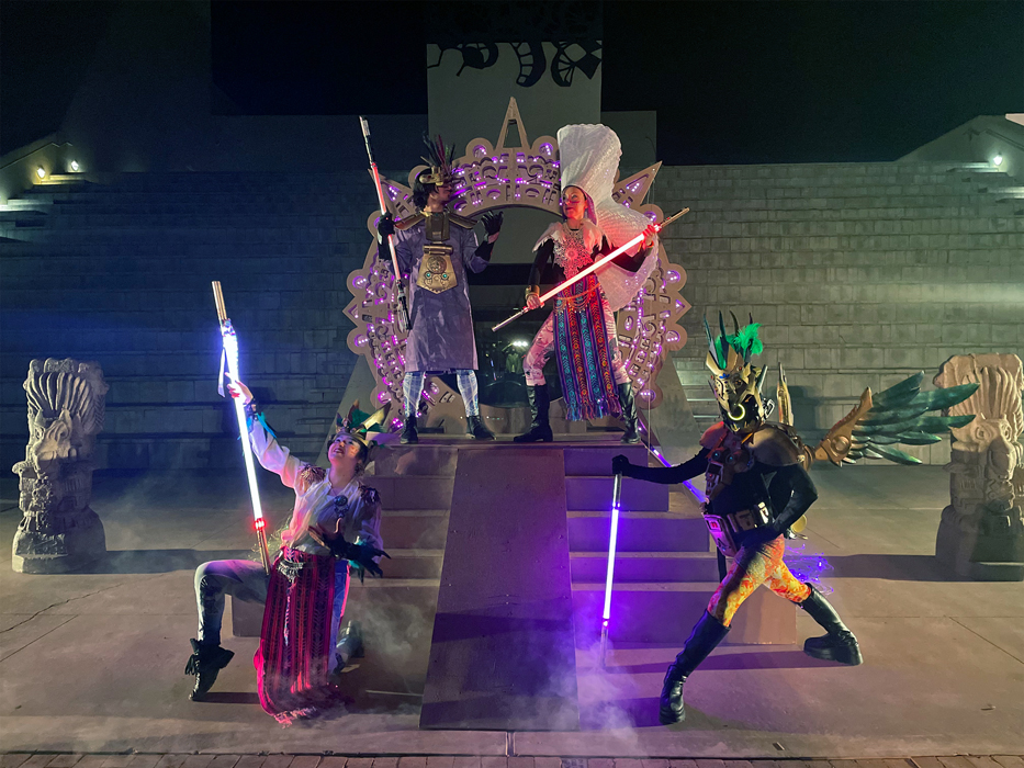 Four people on a stage in Aztec costumes holding swords