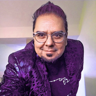 Angel Cabrales facing forward smiling, glasses, purple hair, purple leopard print jacket