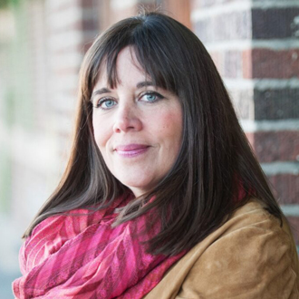 Meta Newhouse is facing forward and smiling. She has long brown hair and wears a pink scarf with a brown jacket.