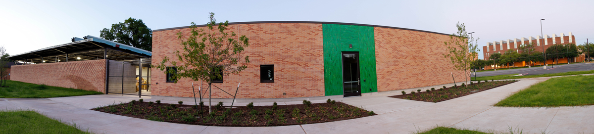 The UNT Art Annex, brown brick building with a green door surround, parking lot and Art Building are in the distance.