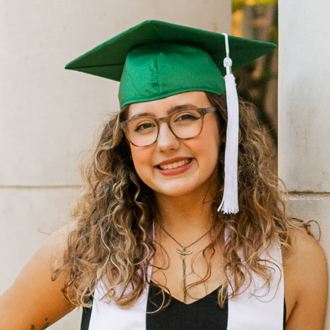 McKenna facing forward, smiling, wearing her graduation cap, long curly hair, brown glasses