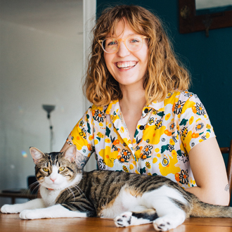 Kristen Barnhart Peers smiling, large tabby cat is lying on a table in front of her.