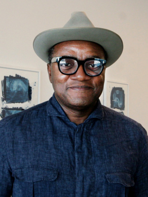 Christopher Blay, man wearing glasses, fedora hat and a dark blue shirt, smiling