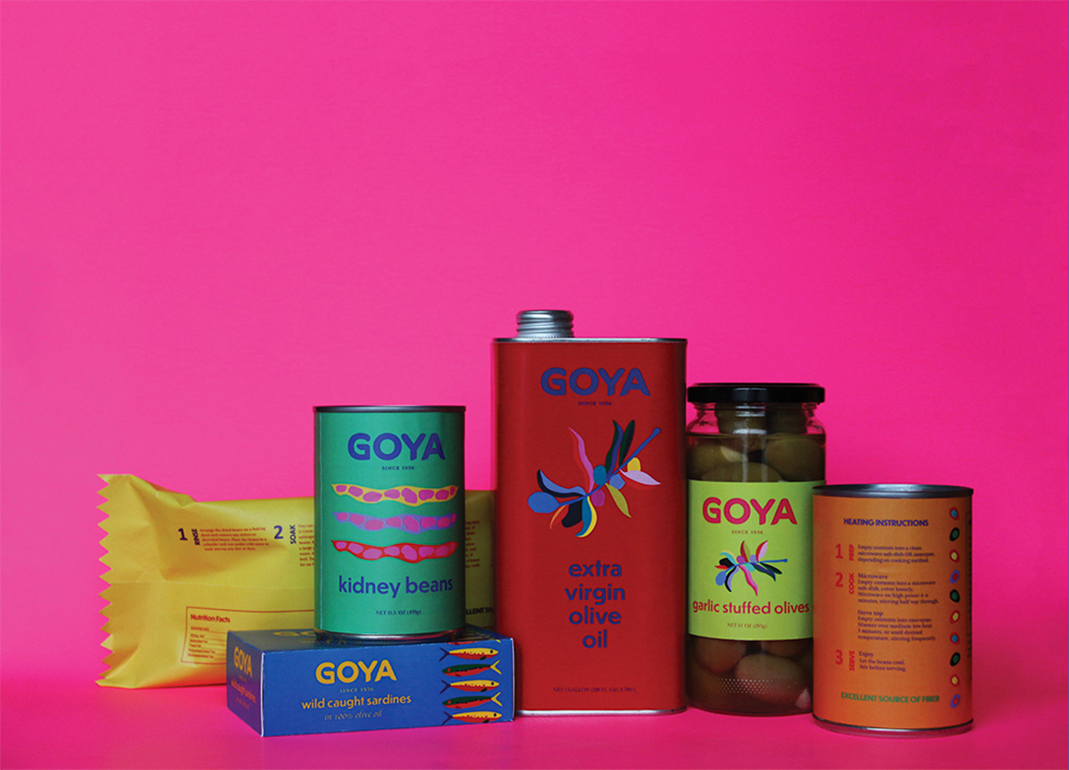 A jar of olives, cans of olive oil and beans, and other items arranged on a pink background.