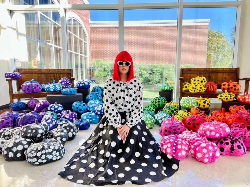 Keisha wearing a bright red wig in front of a window surrounded by colorful artworks