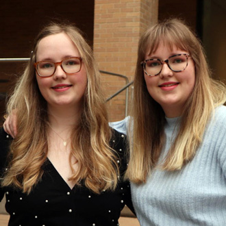 Twins Macey and Mallory Cowden facing forward, blond hair, brown glasses, smiling