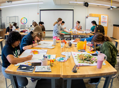 10 Creative U students working on art projects at tables