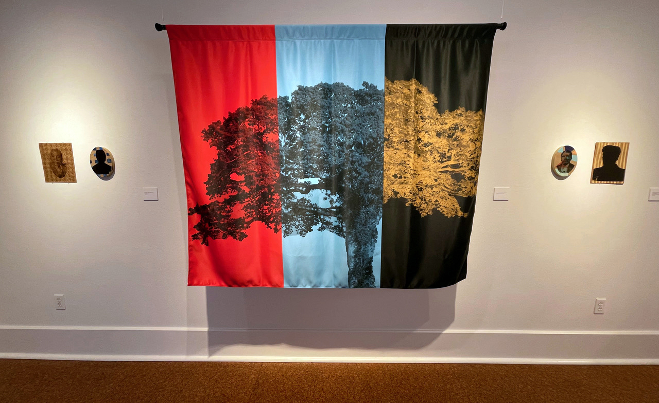Art exhibit of a red, blue and black-striped banner with a tree superimposed on it.