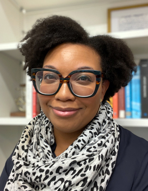 Lauren Cross smiling, wearing glasses, books on shelves in the background