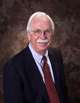 Jack Davis facing forward, smiling, white hair and mustache, wearing a coat and tie.