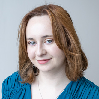 Cuinn facing forward, smiling, shoulder-length red hair, blue top