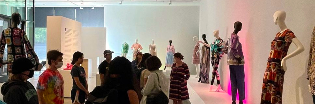 A group of about 10 visitors inside of the CVAD Gallery looking at clothing on mannequins