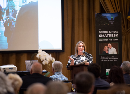 Laura Evans speaking from a podium with an image projected on a screen in the background